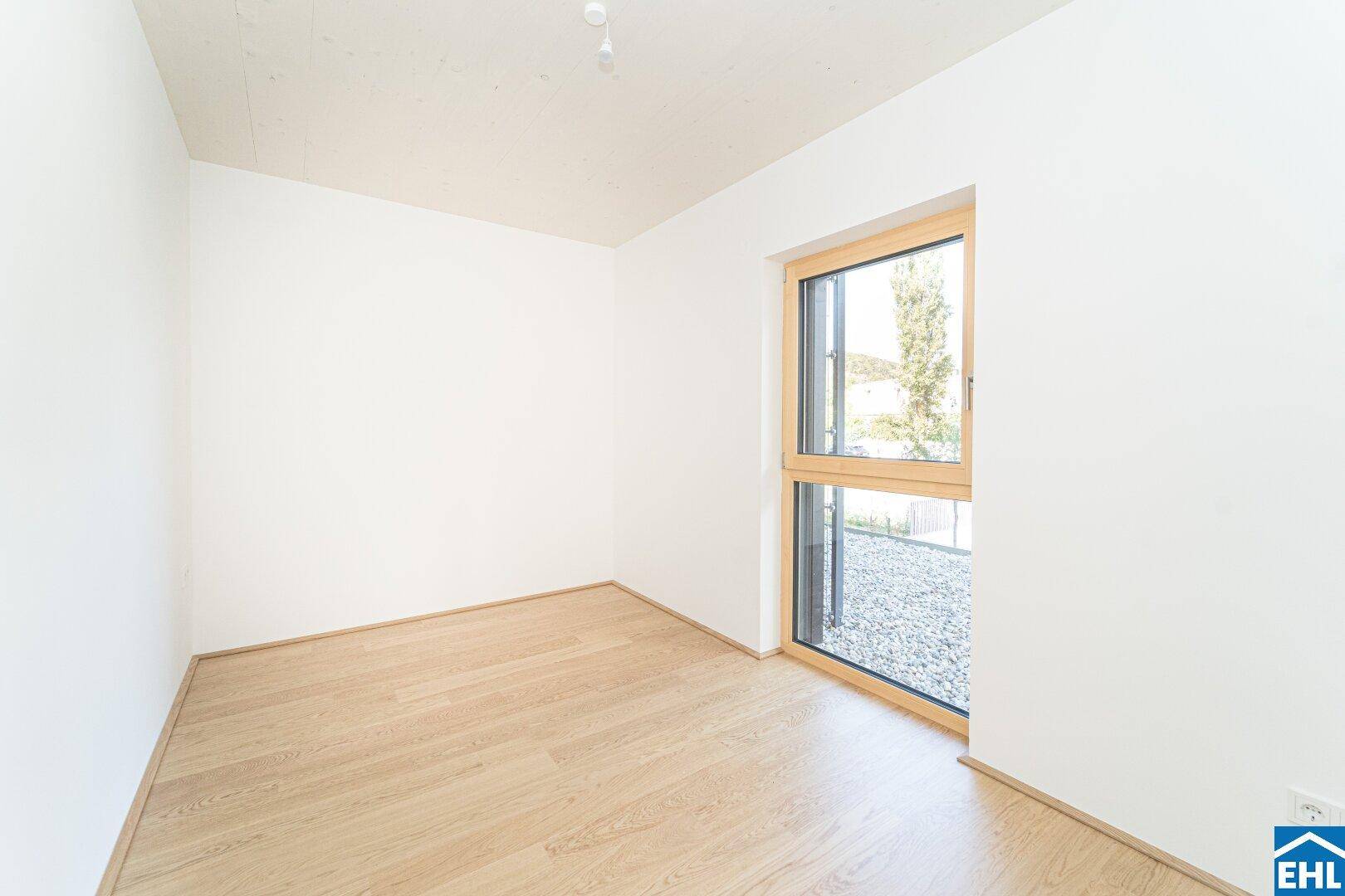 Heller, leerer Raum mit Holzboden und Blick auf einen Kiesbereich, ideal für Ruhe.