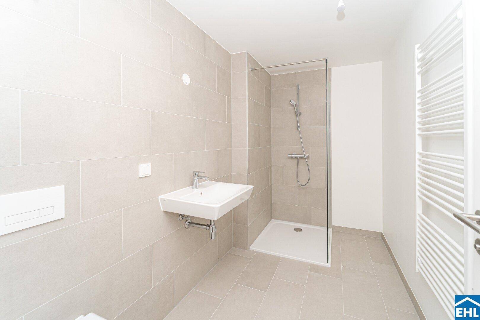 Modernes Badezimmer mit hellen Fliesen, Dusche und beheiztem Handtuchhalter für Komfort.