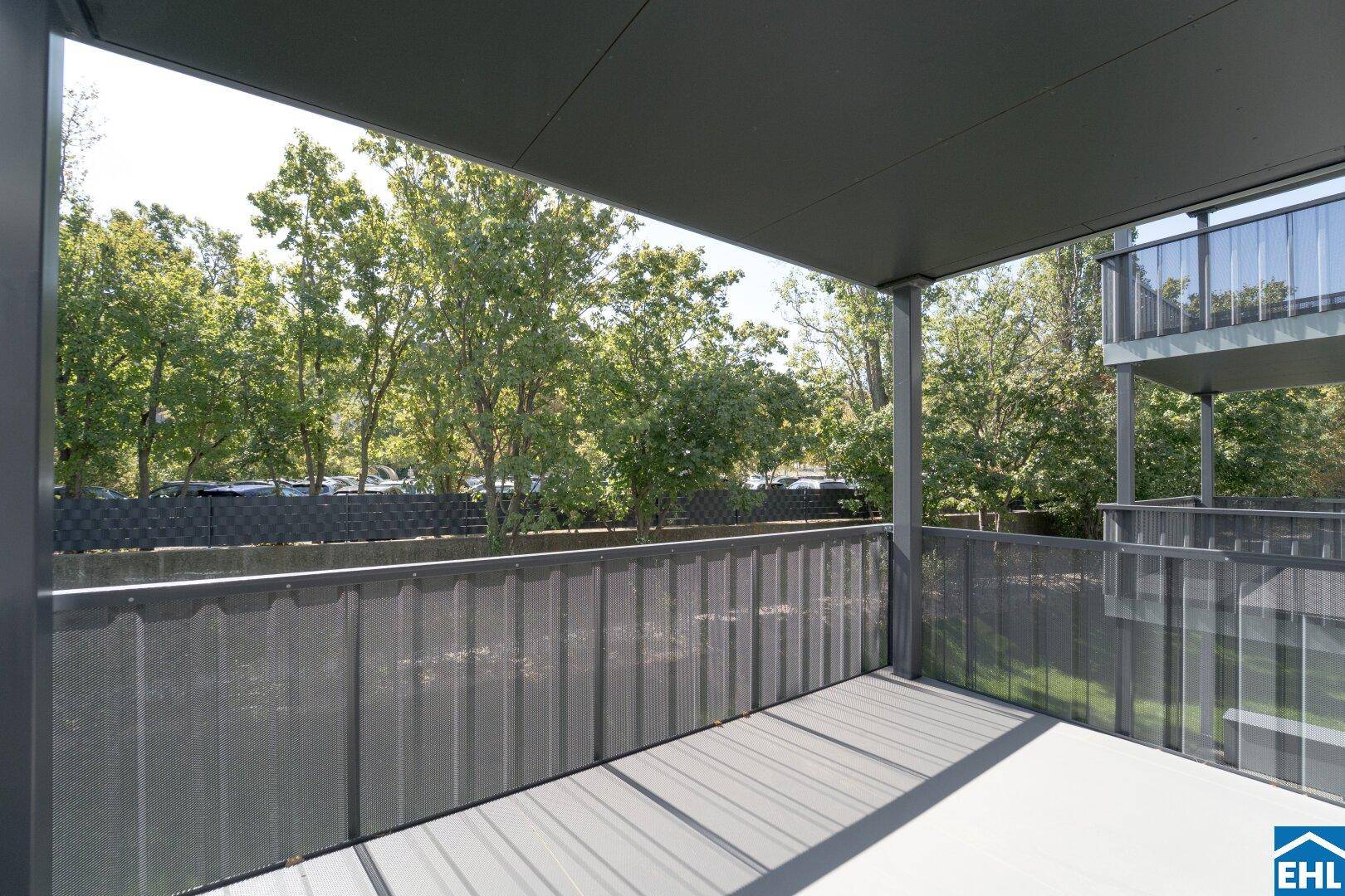 Geräumiger überdachter Balkon mit Blick auf Bäume und Nachbargebäude, bietet Privatsphäre.