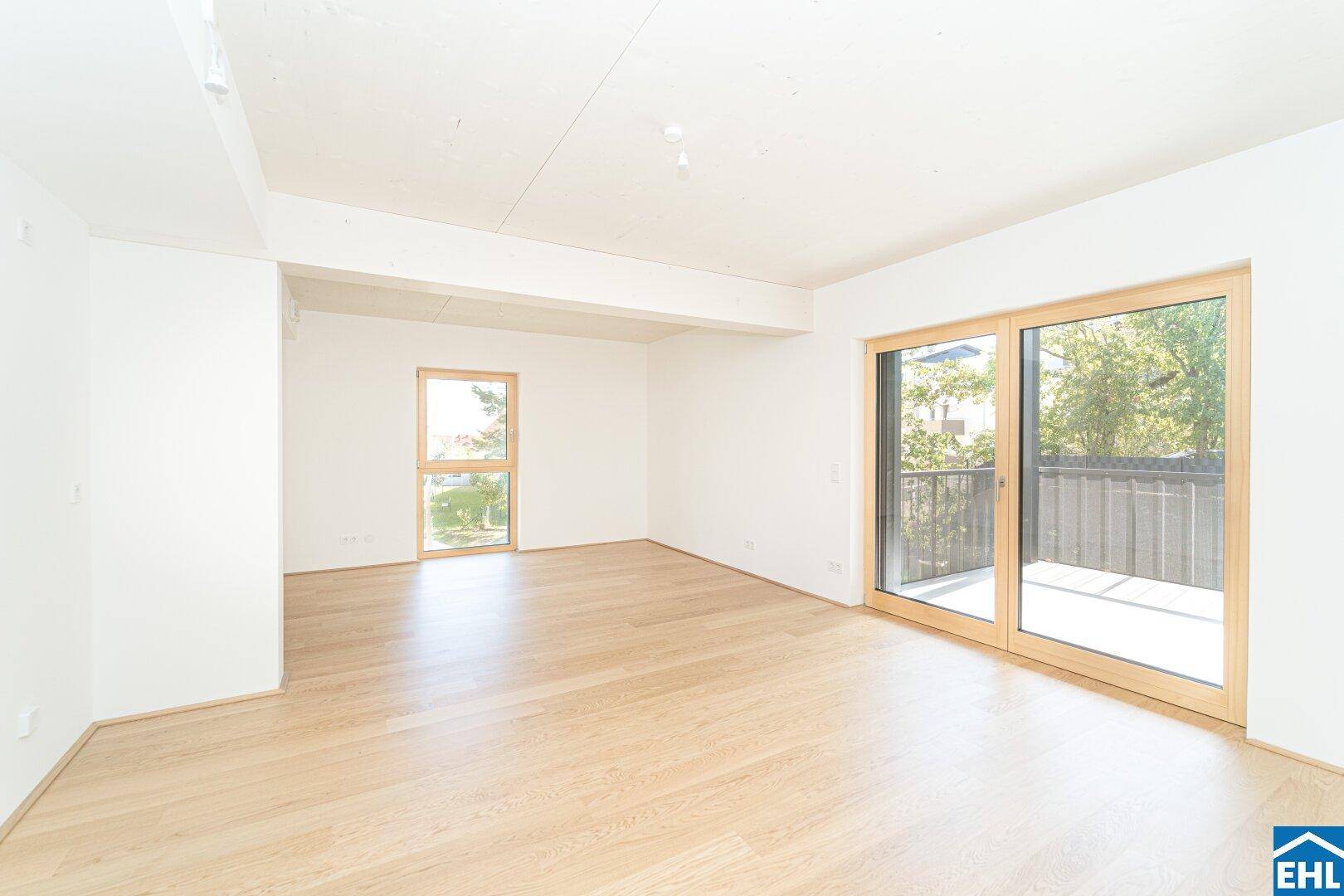 Helles, leeres Zimmer mit Holzboden und Zugang zu einem Balkon, ideal für Wohnbereiche.