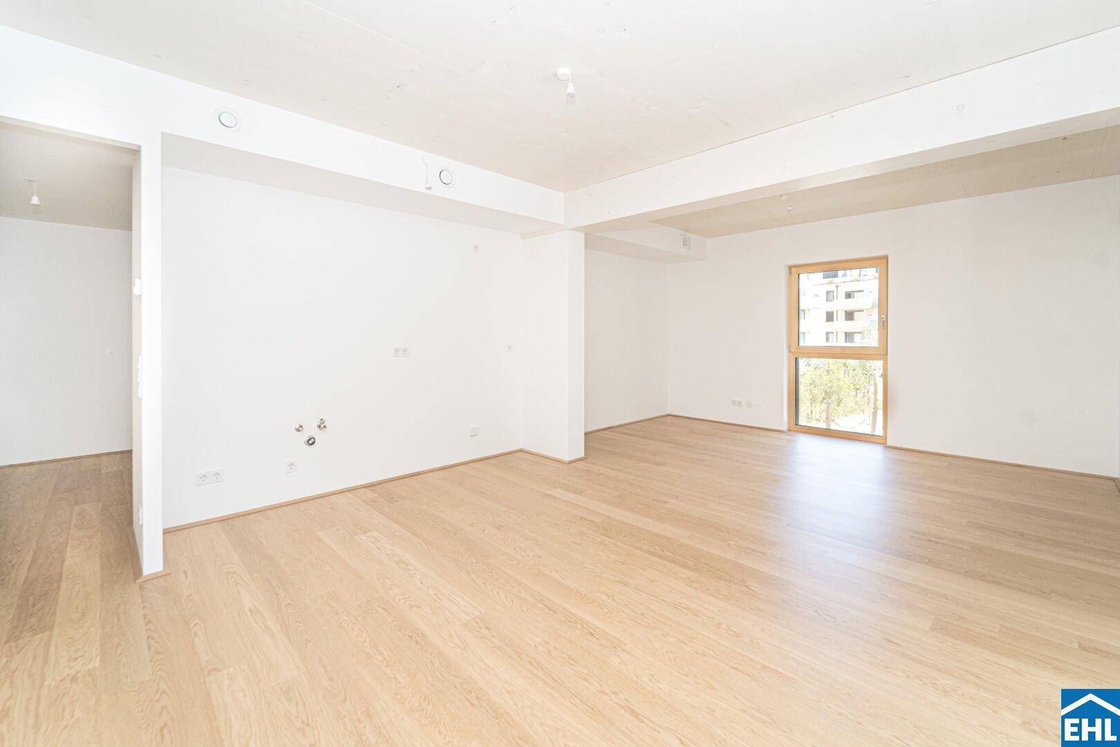 Geräumiges, leeres Zimmer mit Holzboden und großem Fenster, bereit für individuelle Gestaltung.