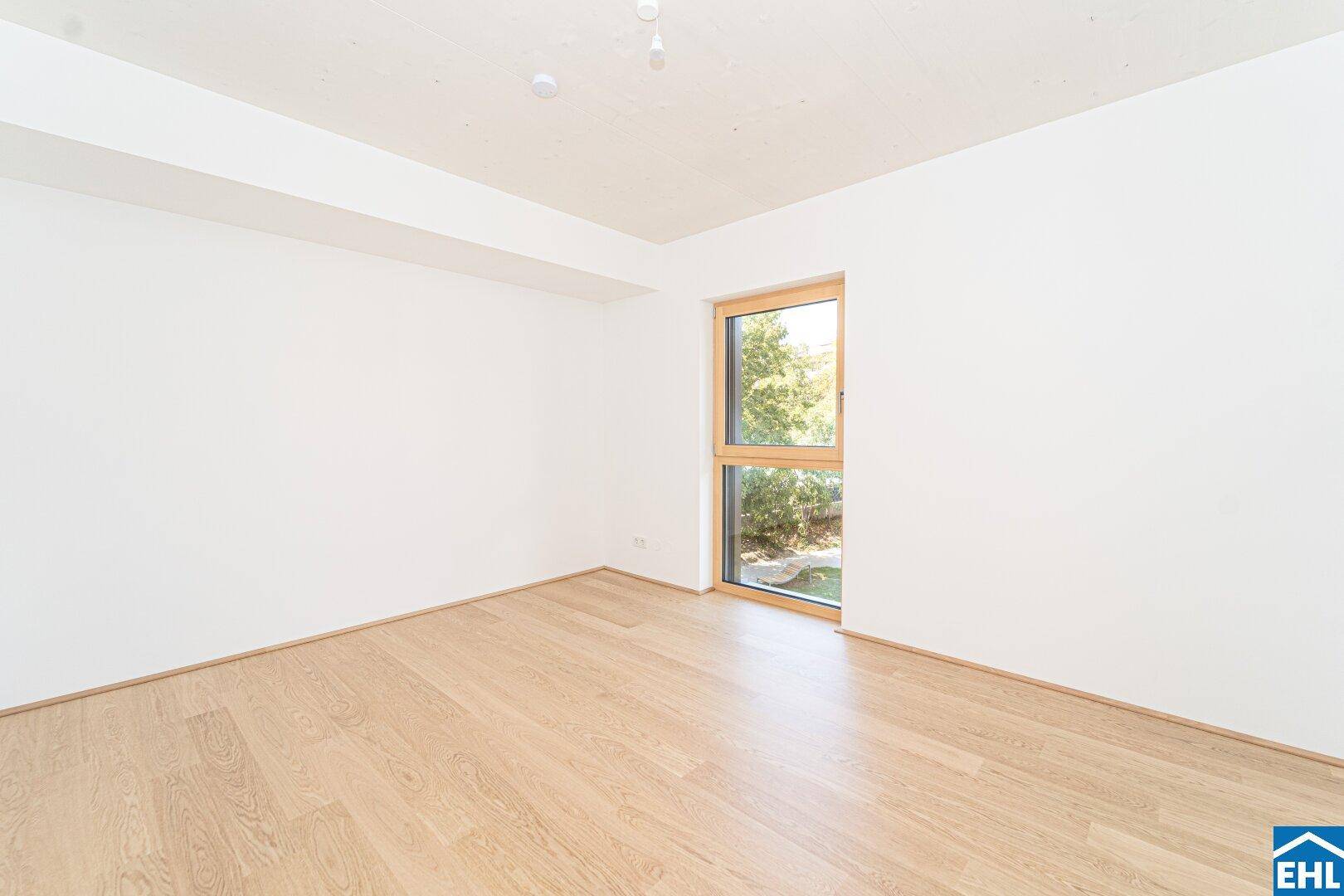 Helles Schlafzimmer mit Holzboden und großem Fenster, das einen ruhigen Blick ins Grüne bietet.