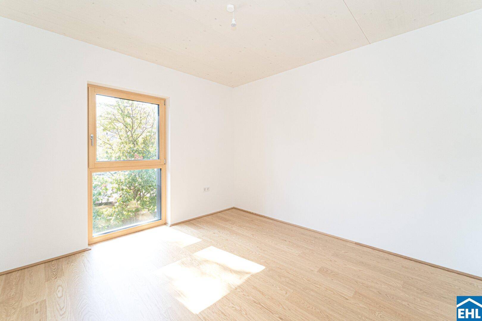 Ruhiges Schlafzimmer mit hellem Holzboden und viel Tageslicht durch das große Fenster.