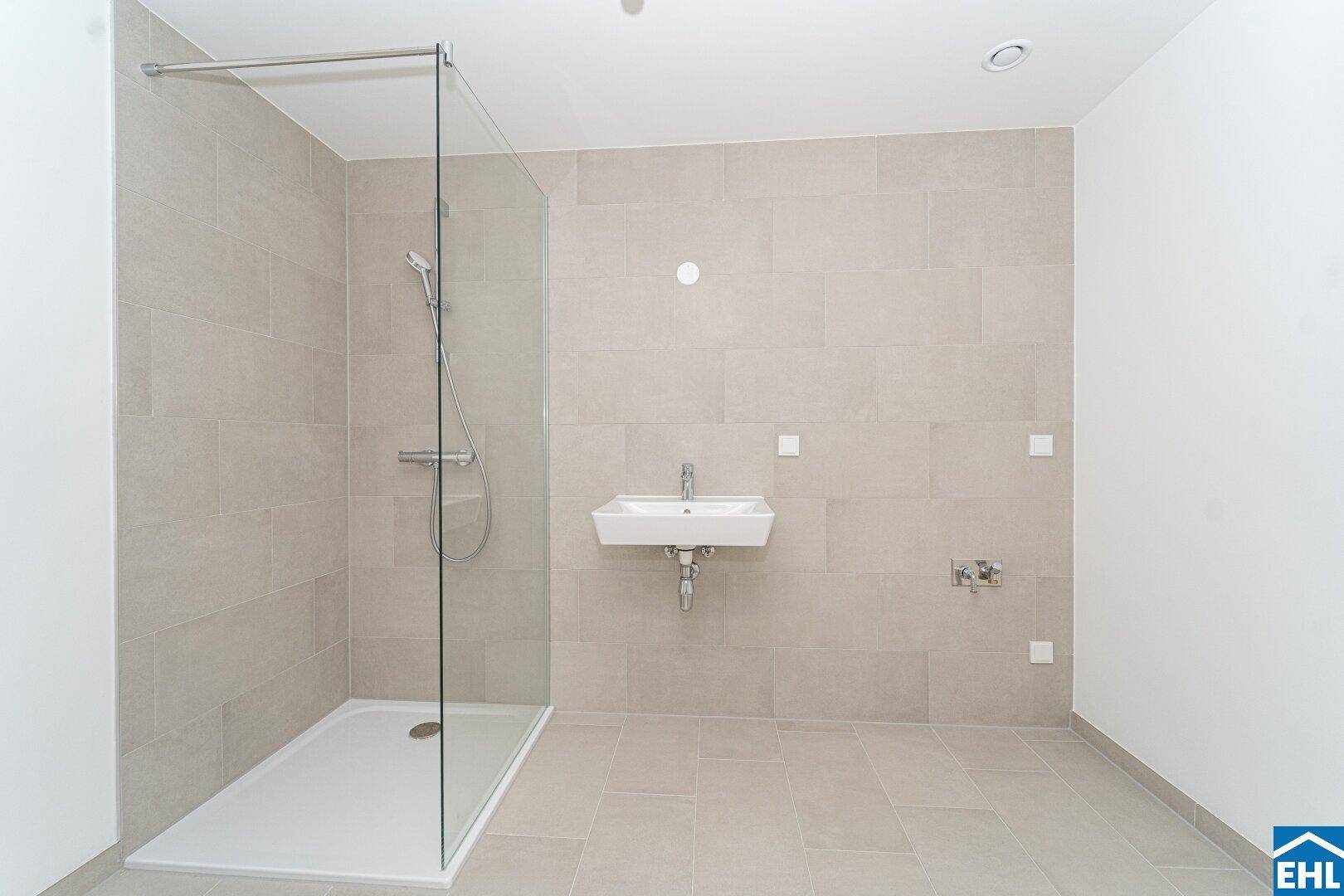 Modernes Badezimmer mit hellgrauen Fliesen, einer begehbaren Dusche und einem Wandwaschbecken.