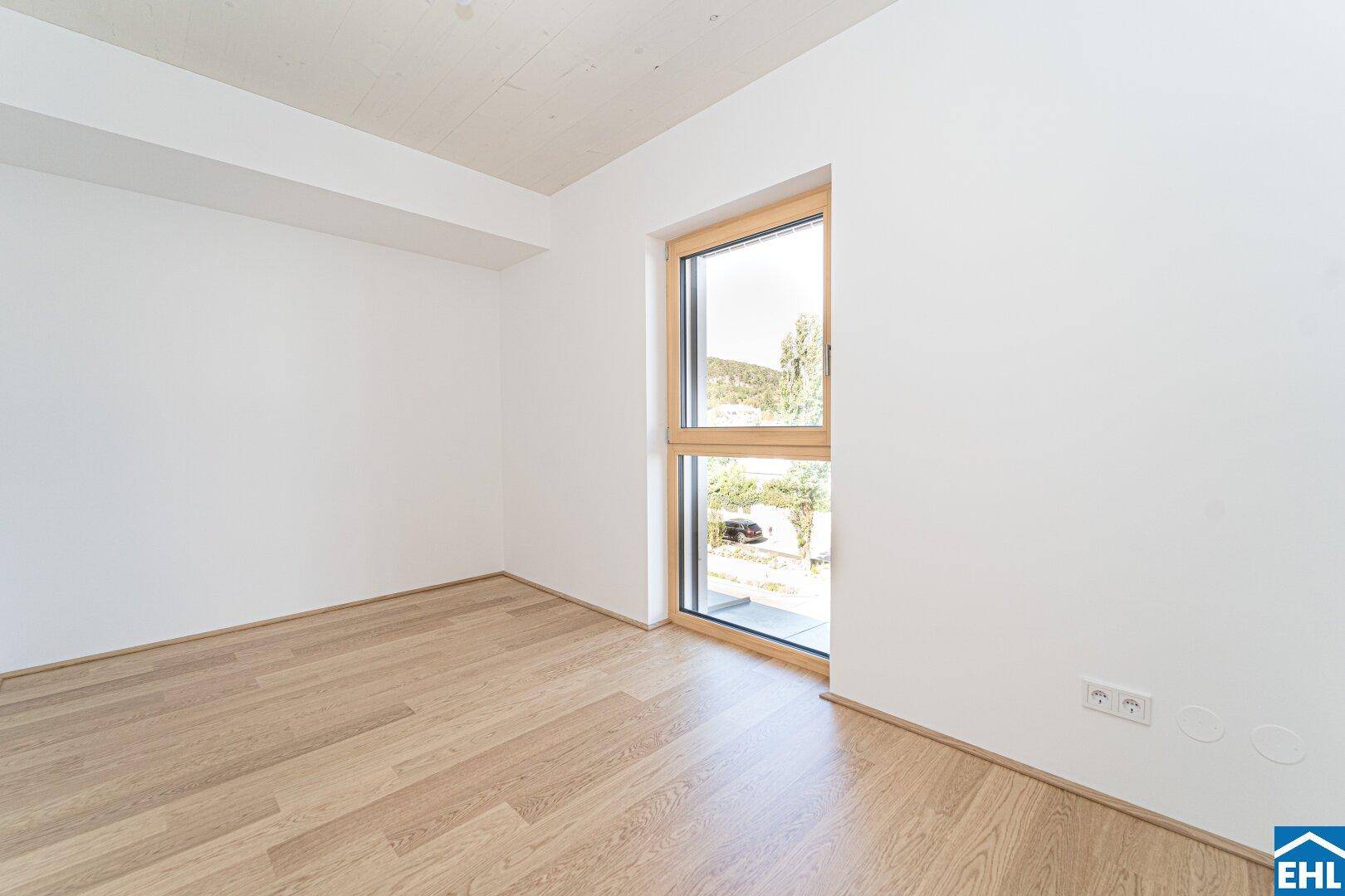 Geräumiges, helles Zimmer mit Holzboden und großem Fenster, bietet viel Tageslicht.