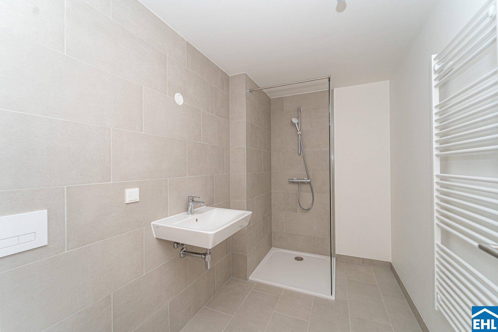 Modernes Badezimmer mit grauen Fliesen, ebenerdiger Dusche, Wand-WC und beheiztem Handtuchhalter.