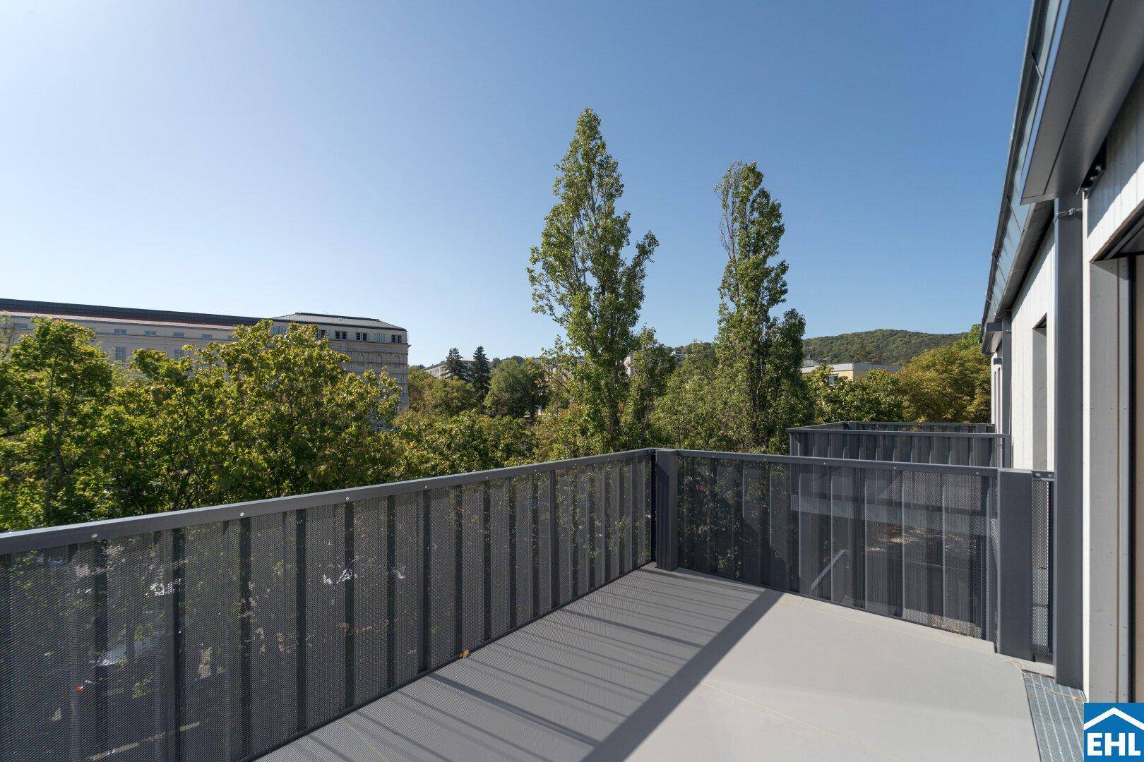 Geräumiger Balkon mit Metallgeländer und Blick auf Bäume und umliegende Gebäude.