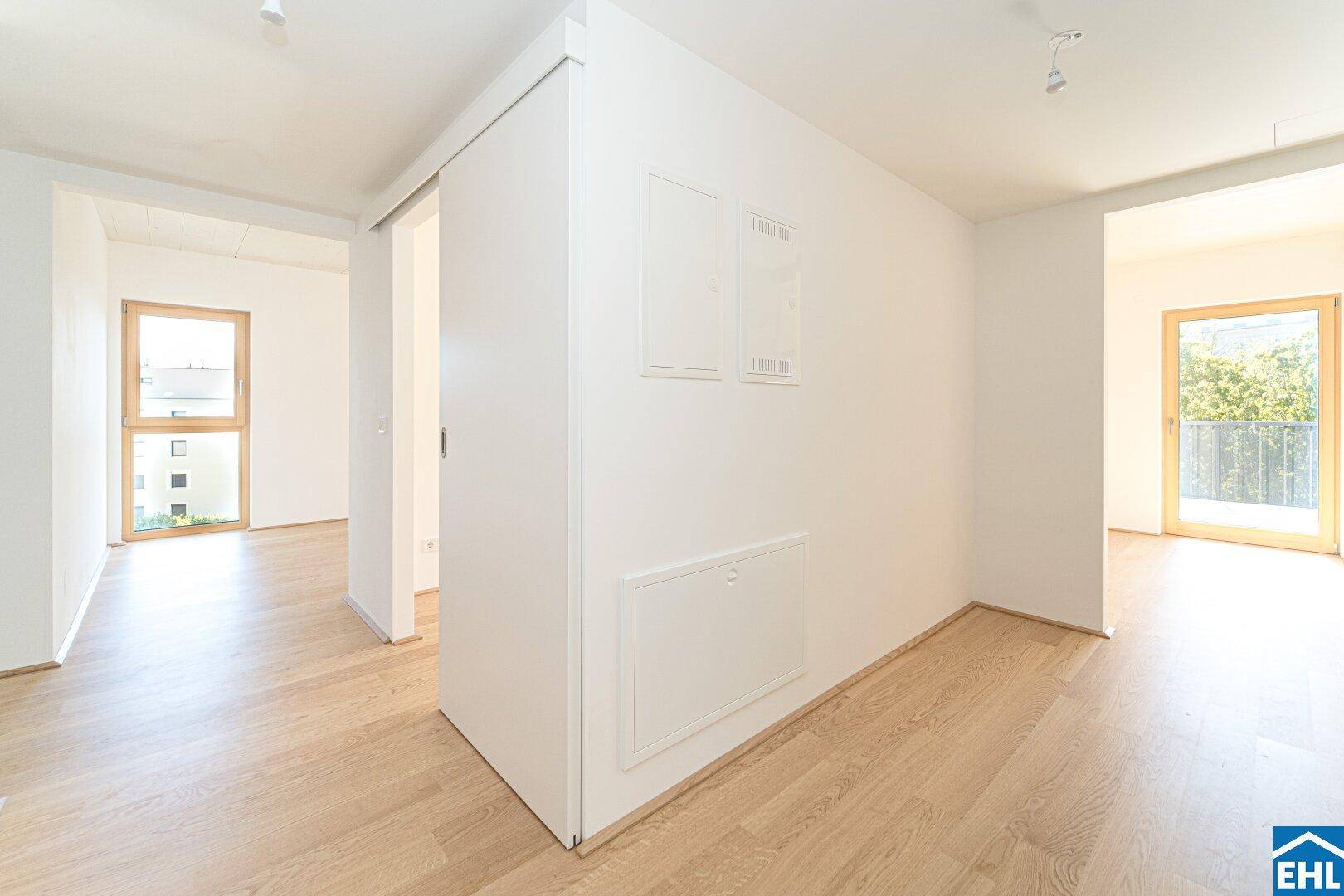 Heller Flurbereich mit Holzboden und weißen Wänden, Schiebetür und Blick in einen weiteren Raum.