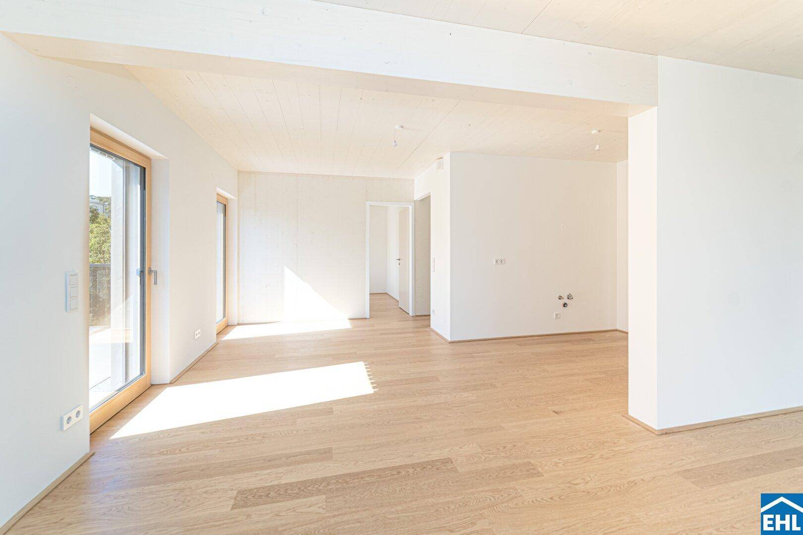 Lichtdurchfluteter Raum mit Holzboden und weißen Wänden, großen Fenstern und Zugang zu einem Außenbereich.
