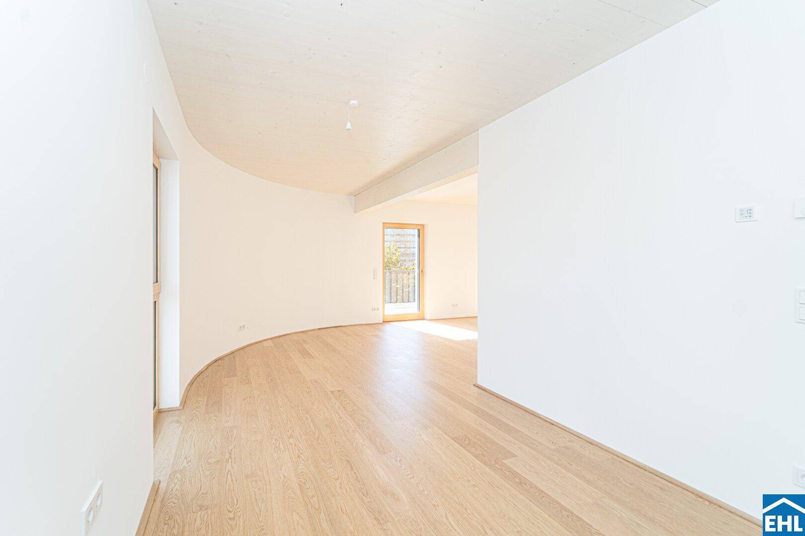 Heller, leerer Raum mit geschwungener Wand, Holzboden und Zugang zu einem Außenbereich, ideal für individuelle Gestaltung.