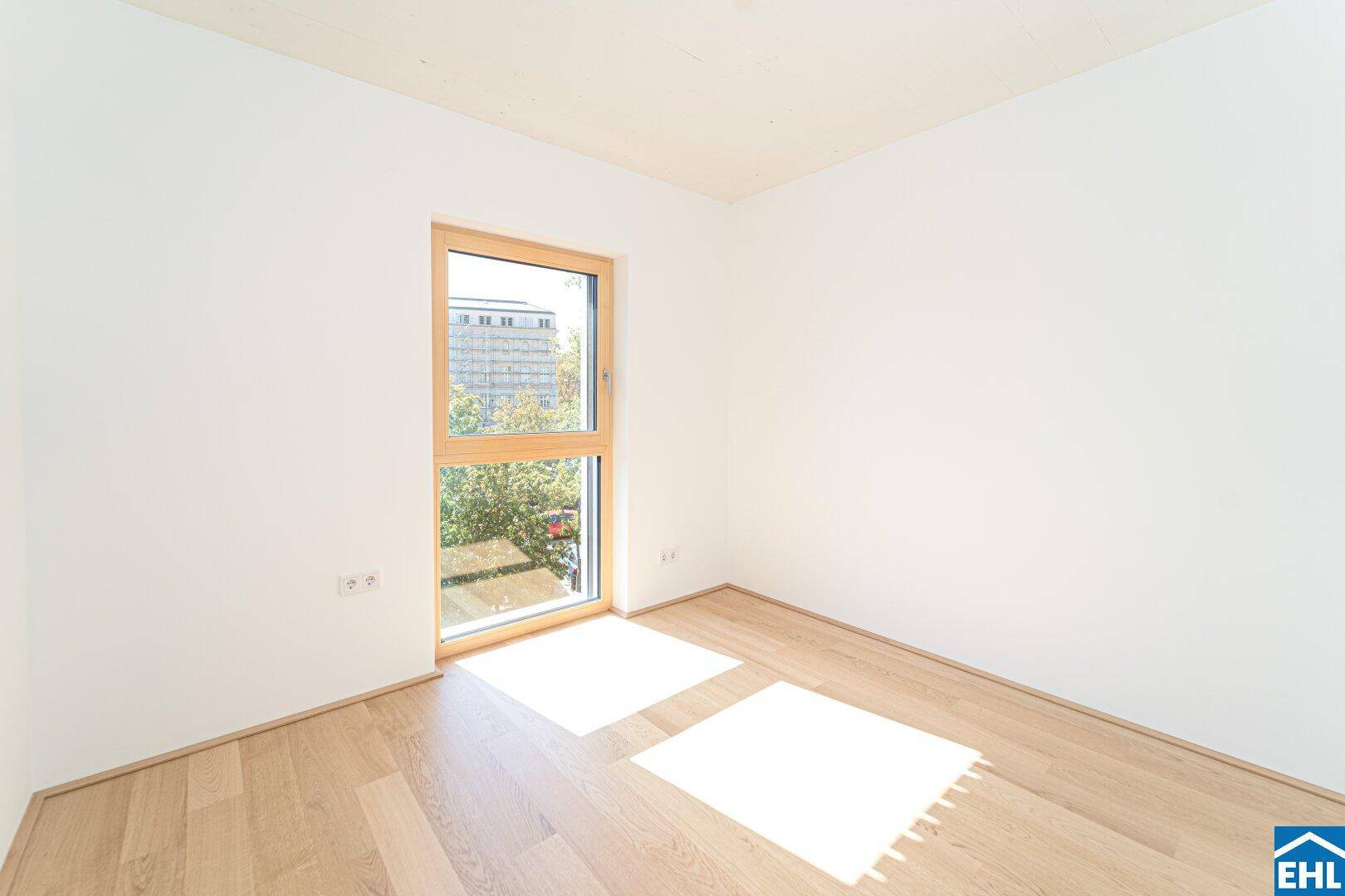 Lichtdurchflutetes Schlafzimmer mit Holzboden, weißen Wänden und einem großen Fenster mit Sonnenlicht.