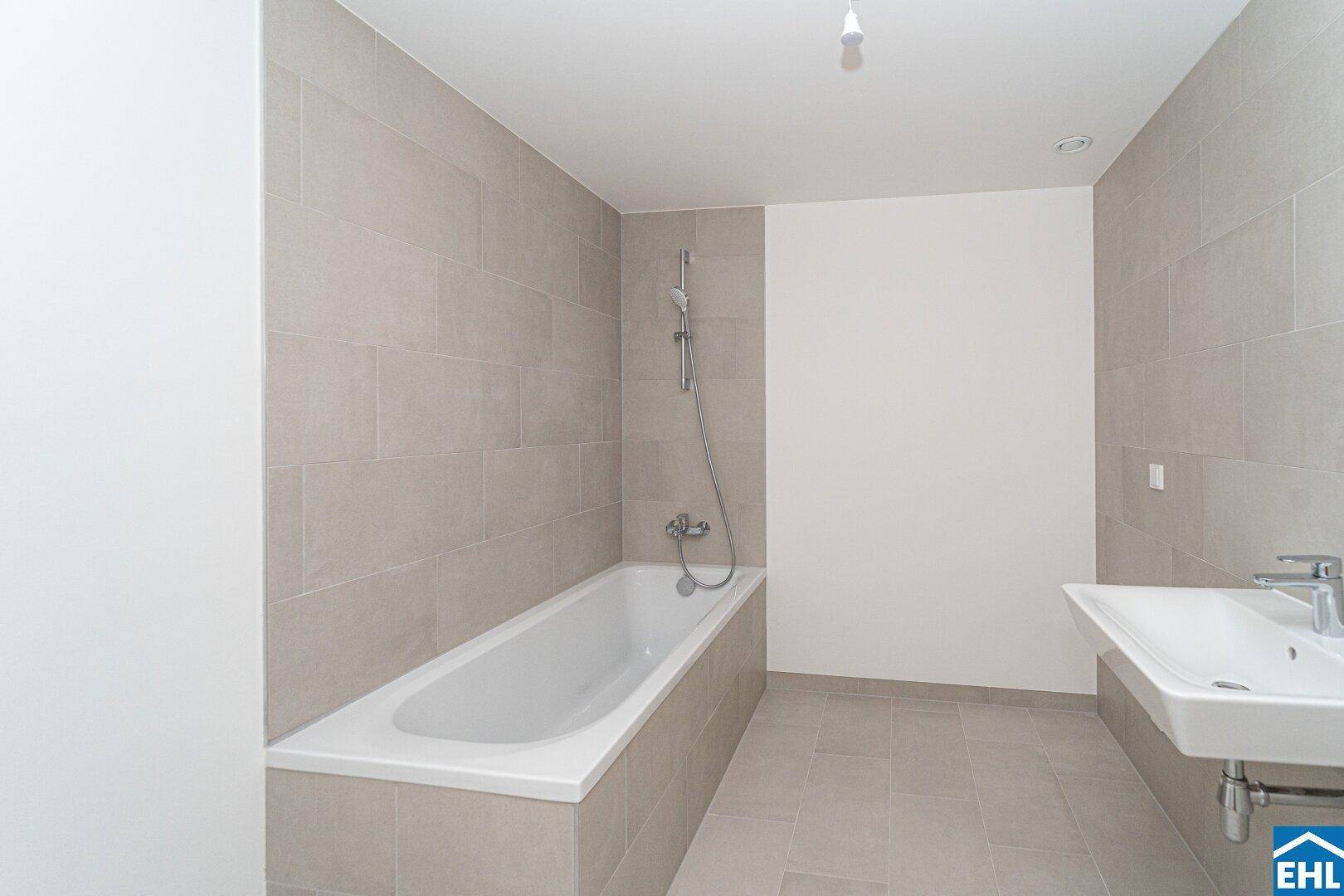 Modernes Badezimmer mit hellgrauen Fliesen, einer Badewanne und einem Einzelwaschbecken.