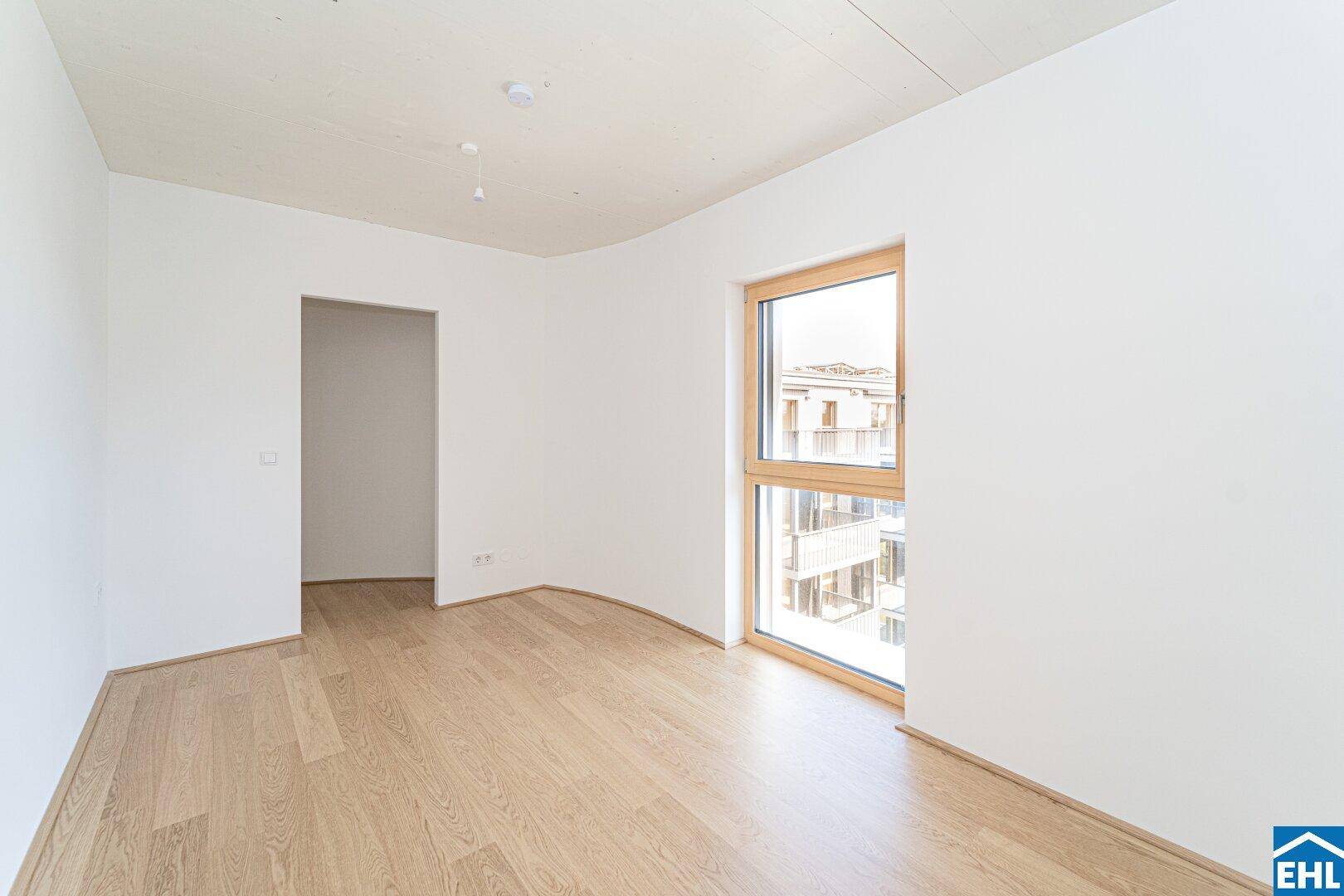Helles Schlafzimmer mit Holzboden, weißen Wänden und einem großen Fenster, das viel Licht spendet.