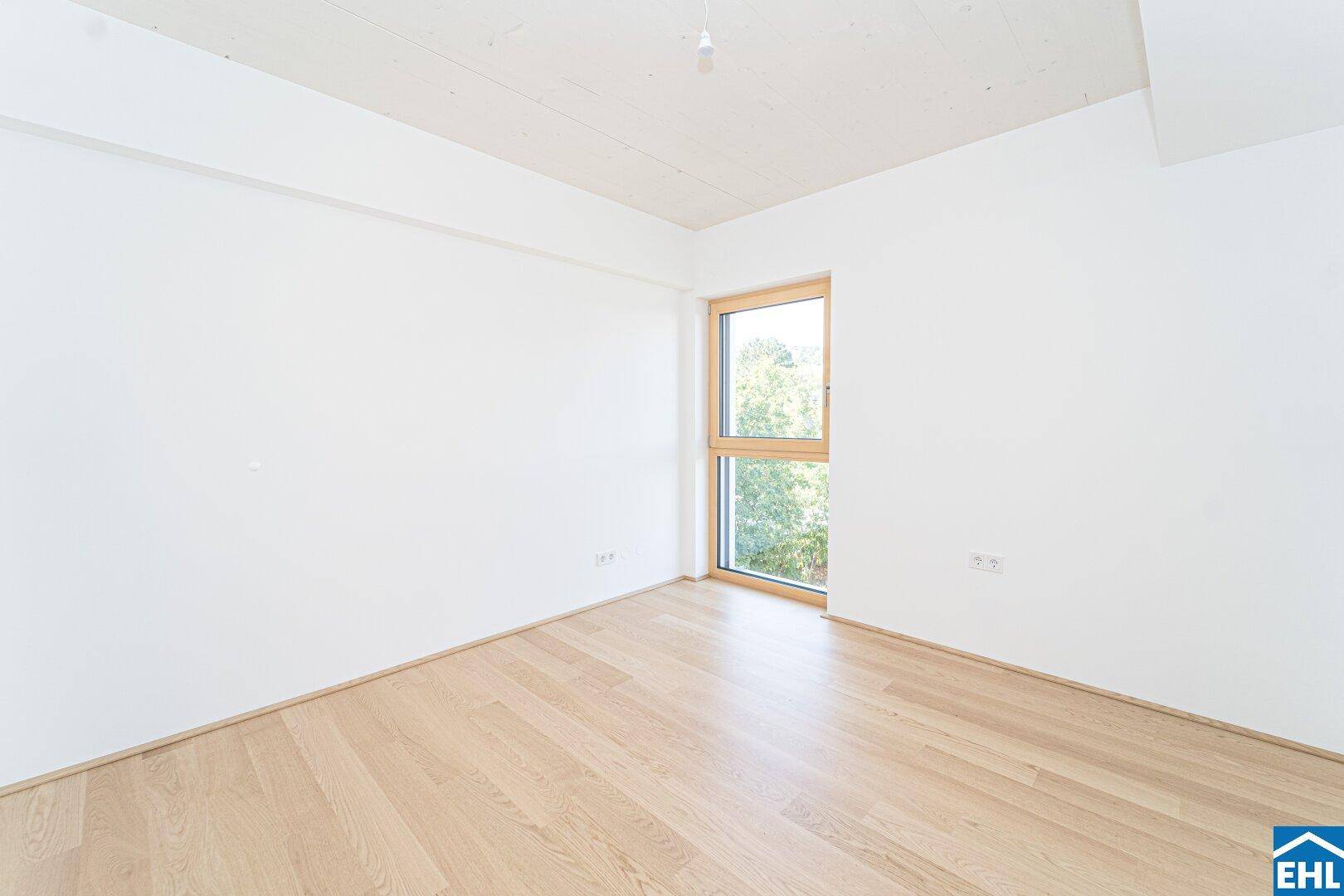 Helles Zimmer mit Holzboden und großem Fenster, ideal als Schlafzimmer oder Büro nutzbar.