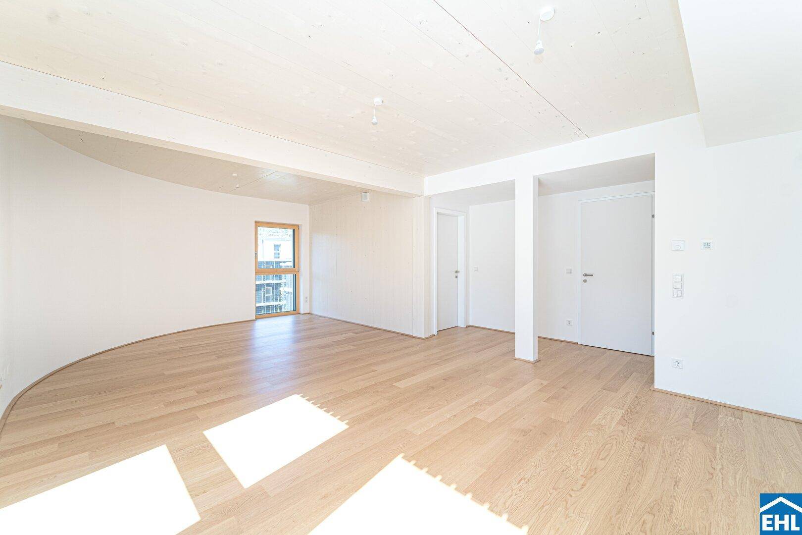 Geräumiger Wohnbereich mit heller Holzdecke, Parkettboden und modernen weißen Türen.