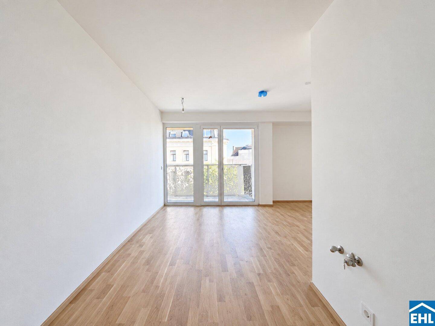 Heller Raum mit Parkettboden und großen Fenstern, die viel Tageslicht hereinlassen und einen Balkonblick bieten.
