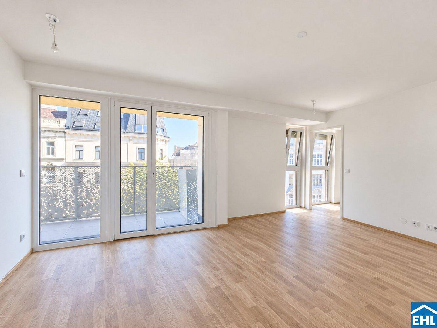 Geräumiges, helles Zimmer mit Parkettboden und großen Fenstern, die zu einem Balkon führen.