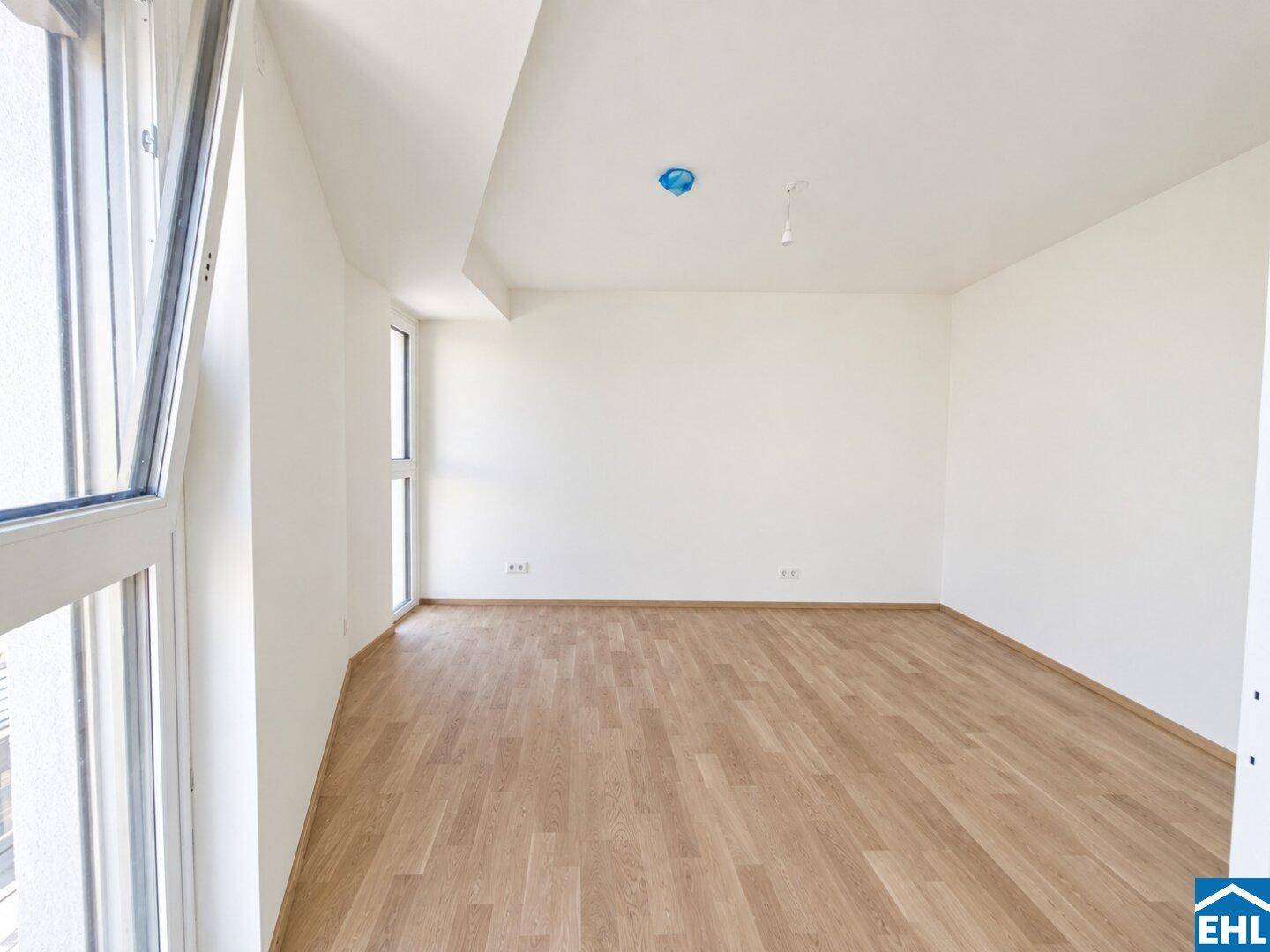 Helles Zimmer mit Parkettboden und einem Eckfenster, das eine gute Belichtung des Raumes ermöglicht.