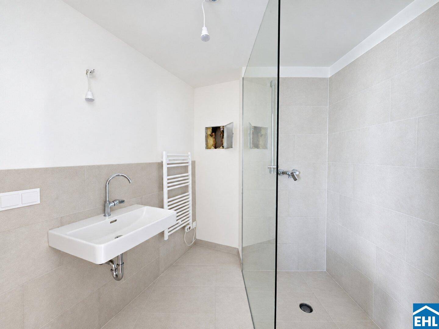 Modernes Badezimmer mit begehbarer Dusche, Einzelwaschbecken und beheiztem Handtuchhalter in hellgrauen Fliesen.
