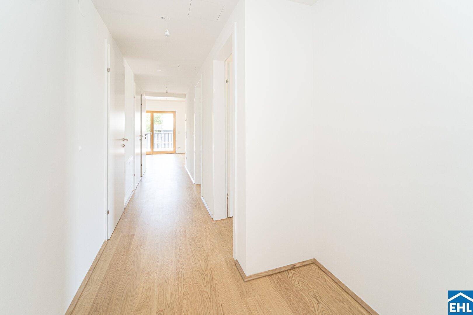 Langer, heller Flur mit mehreren Türen und durchgehendem Holzfußboden.