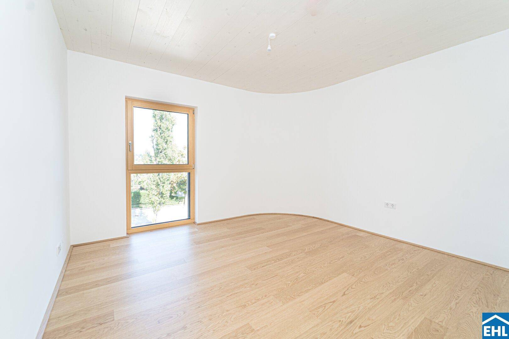 Helles Schlafzimmer mit Parkettboden und einem großen Fenster mit Blick ins Grüne.