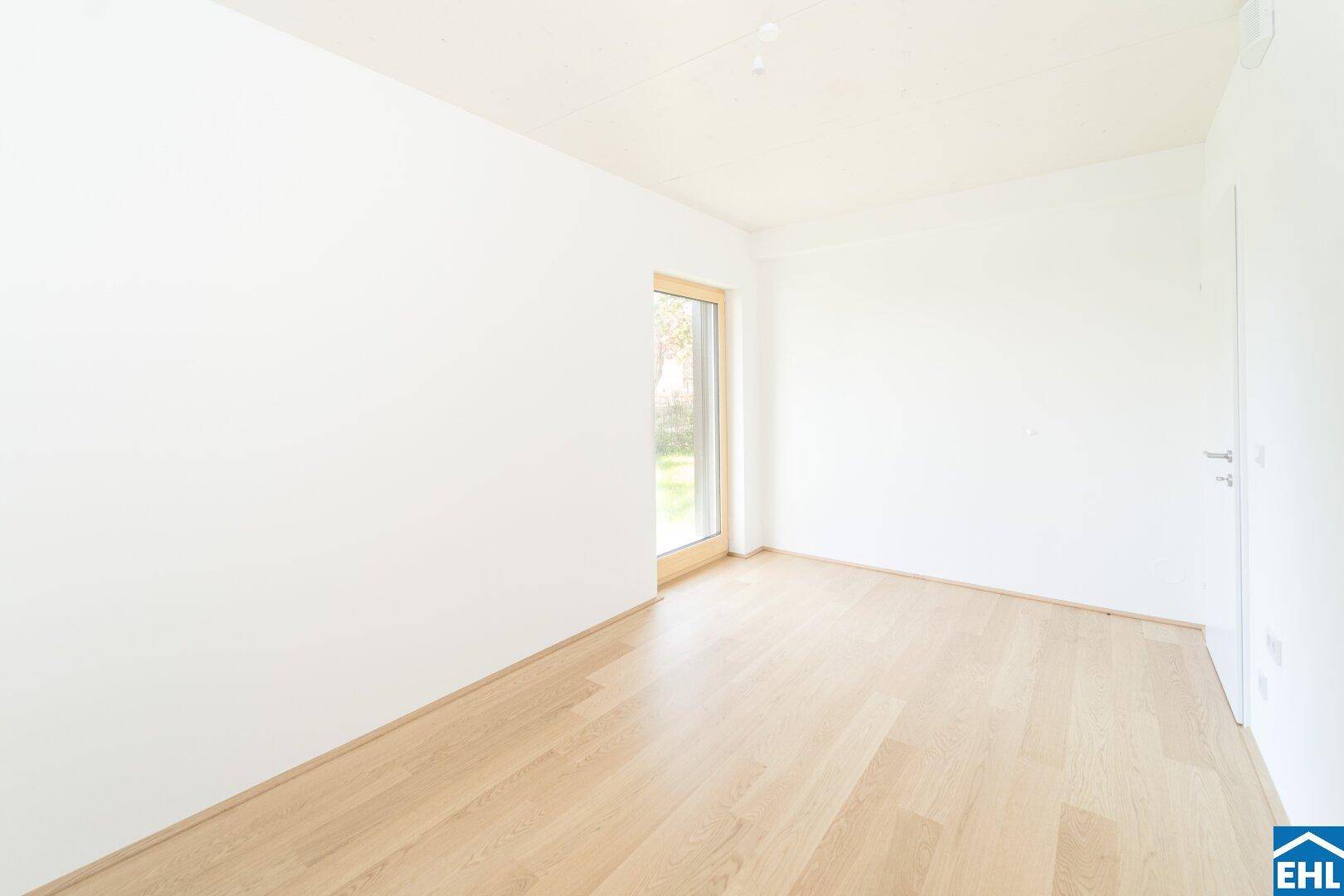 Kleinerer, heller Raum mit Holzboden und einem Fenster mit Blick ins Grüne.