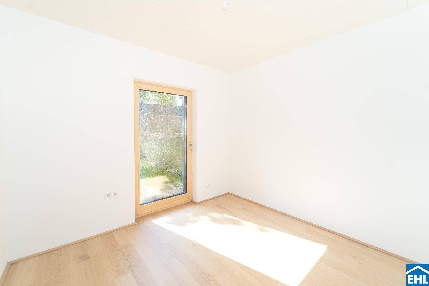 Heller Raum mit Holzboden und einem großen Fenster, das viel Tageslicht hereinlässt.