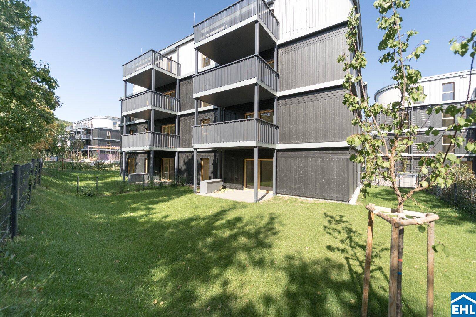 Moderne Wohnanlage mit dunkler Holzfassade und gepflegter Rasenfläche im Gartenbereich.