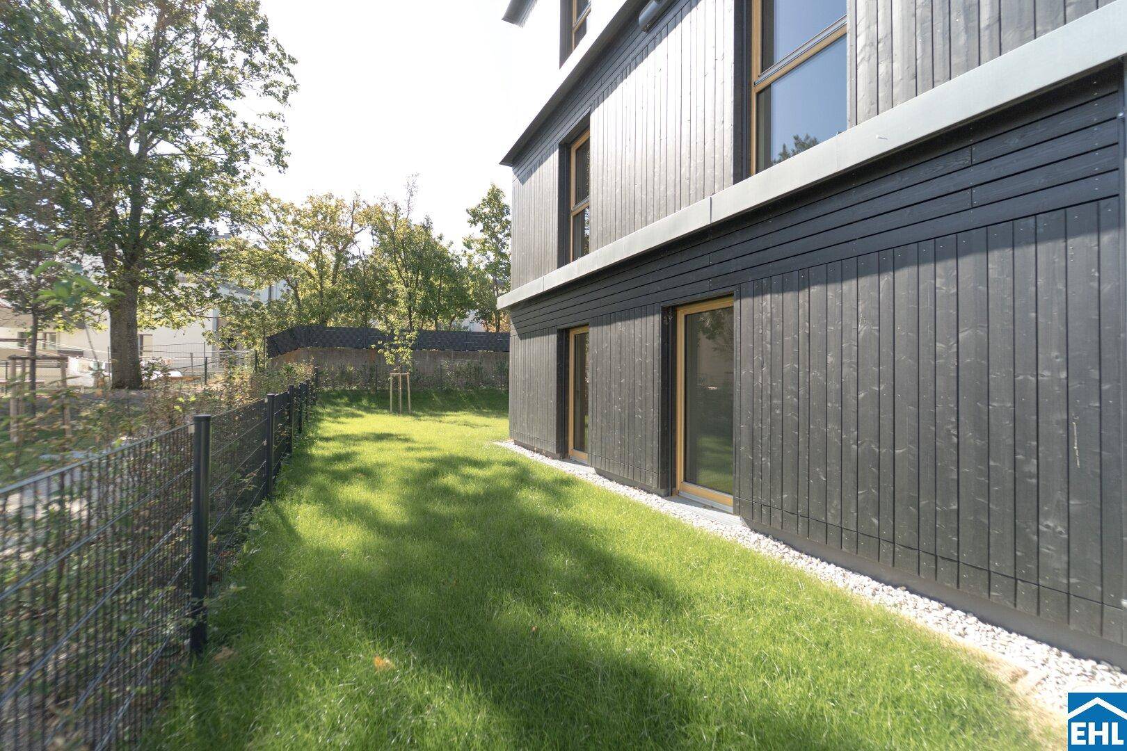 Seitlicher Gartenbereich eines modernen Gebäudes mit dunkler Holzfassade und Rasenfläche.