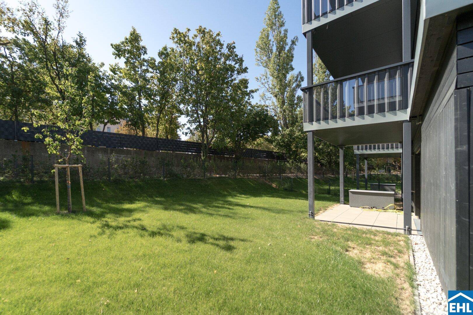 Gepflegter Gartenbereich mit Rasen und einer kleinen Terrasse vor dem modernen Gebäude.