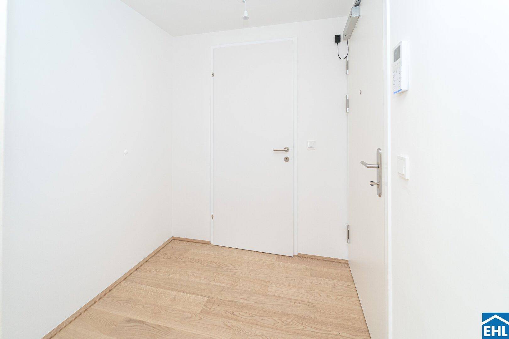 Eingangsbereich mit Holzboden, weißen Türen und einer modernen Gegensprechanlage.