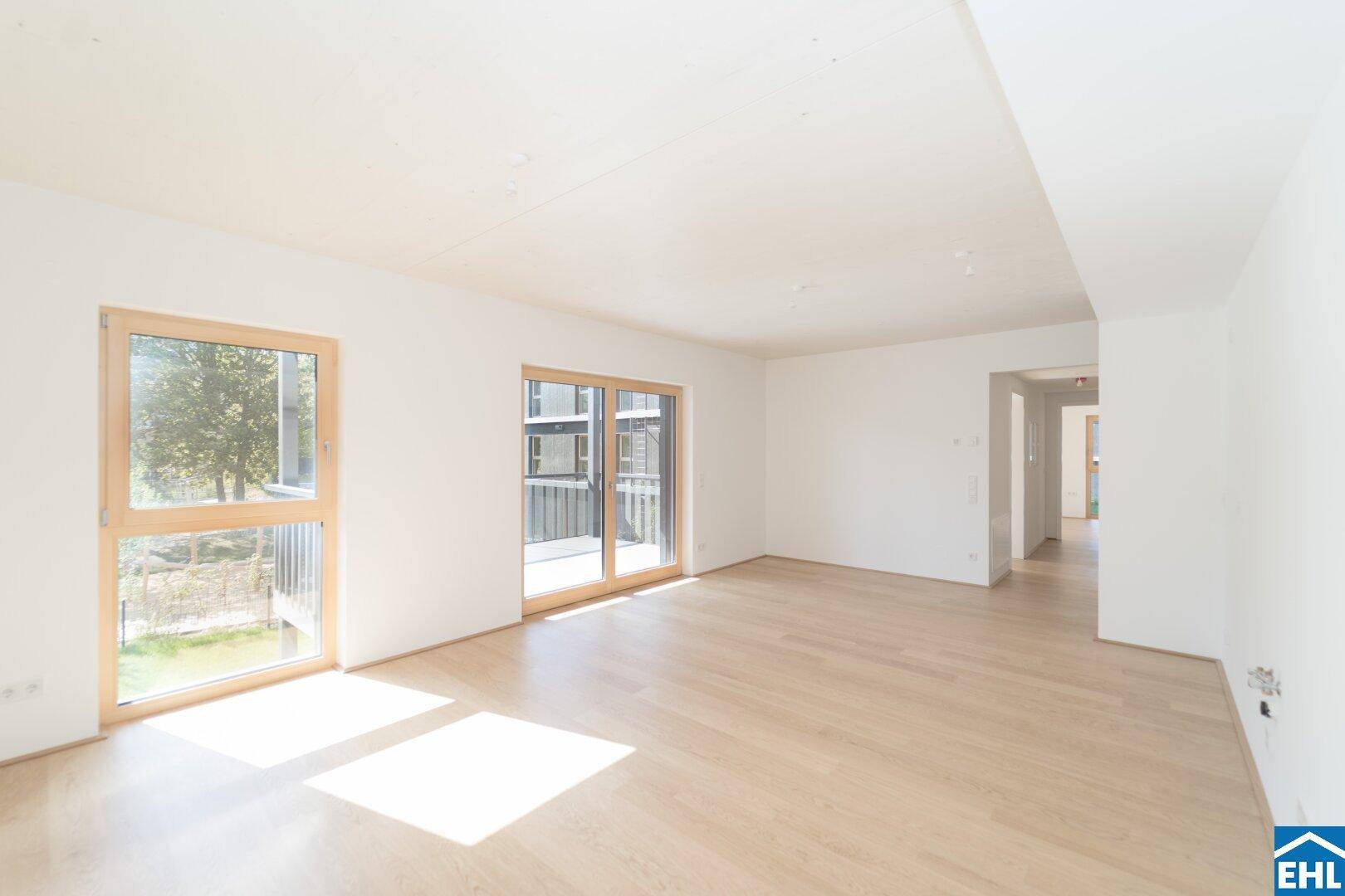 Geräumiges Wohnzimmer mit viel Tageslicht, hellem Parkettboden und Zugang zu weiteren Räumen.
