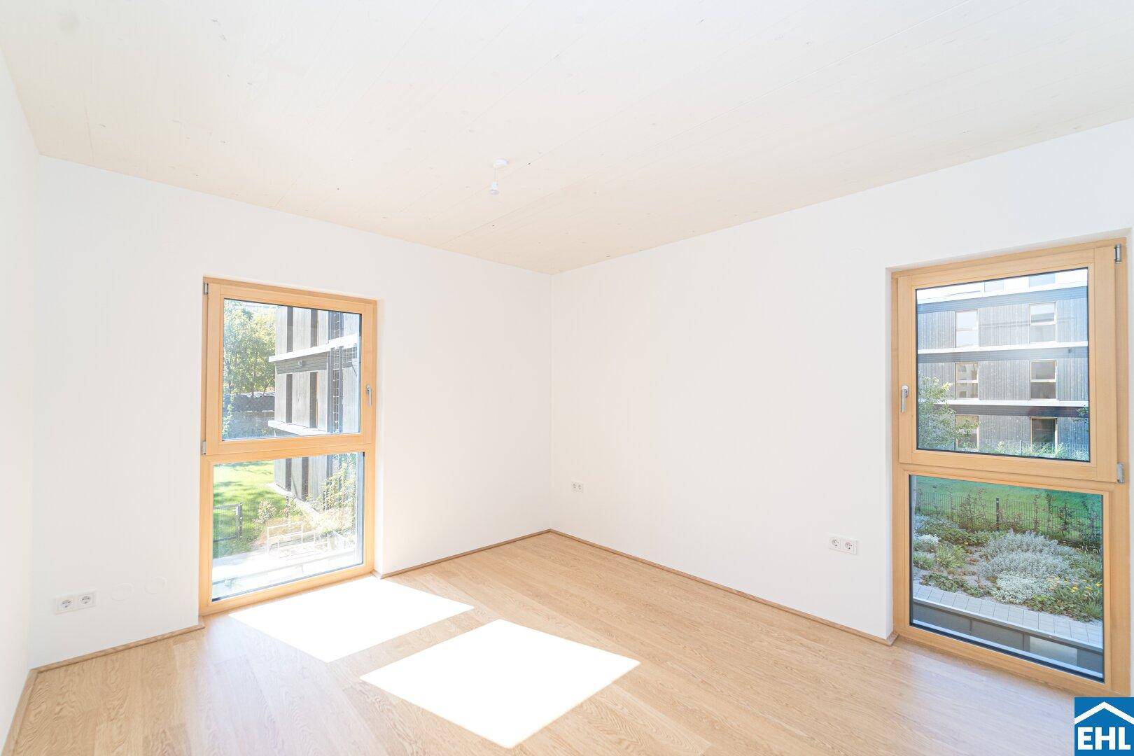 Helles Zimmer mit Holzboden und zwei großen Fenstern, die viel Tageslicht hereinlassen.