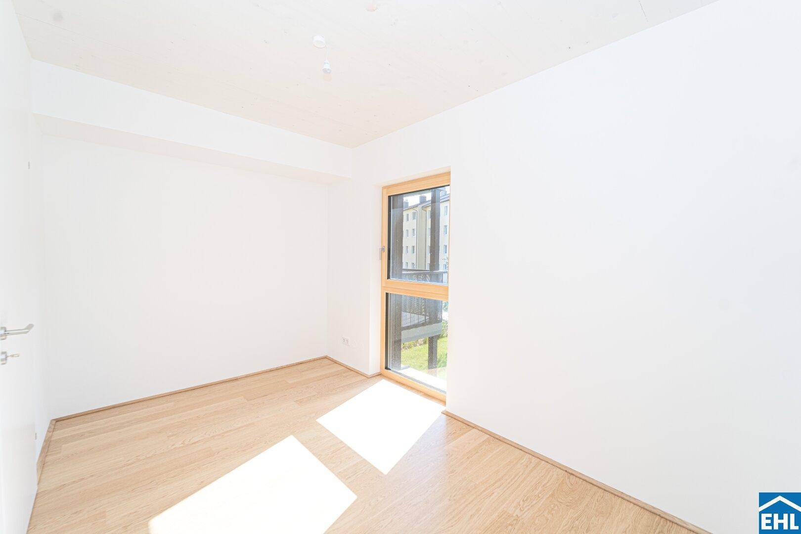 Freundliches Zimmer mit hellem Parkettboden und einem großen Fenster für natürliche Belichtung.