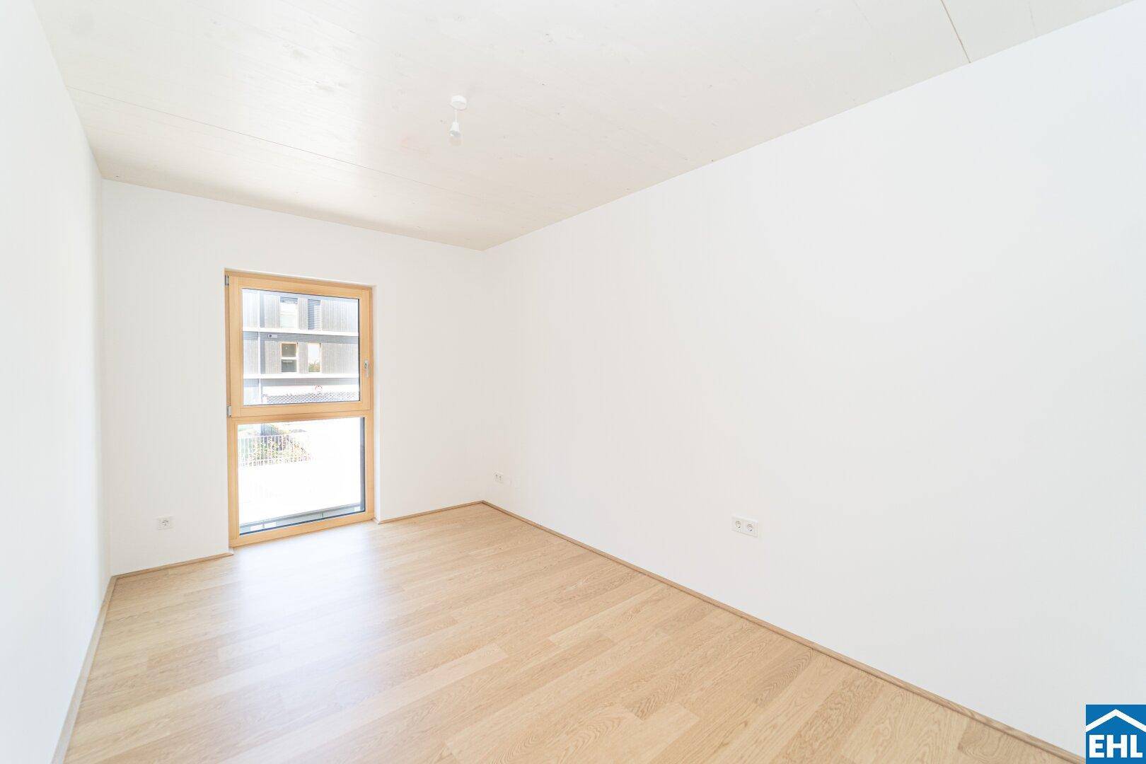 Leeres Zimmer mit hellem Holzfußboden und einem Fenster, das den Raum mit Licht füllt.