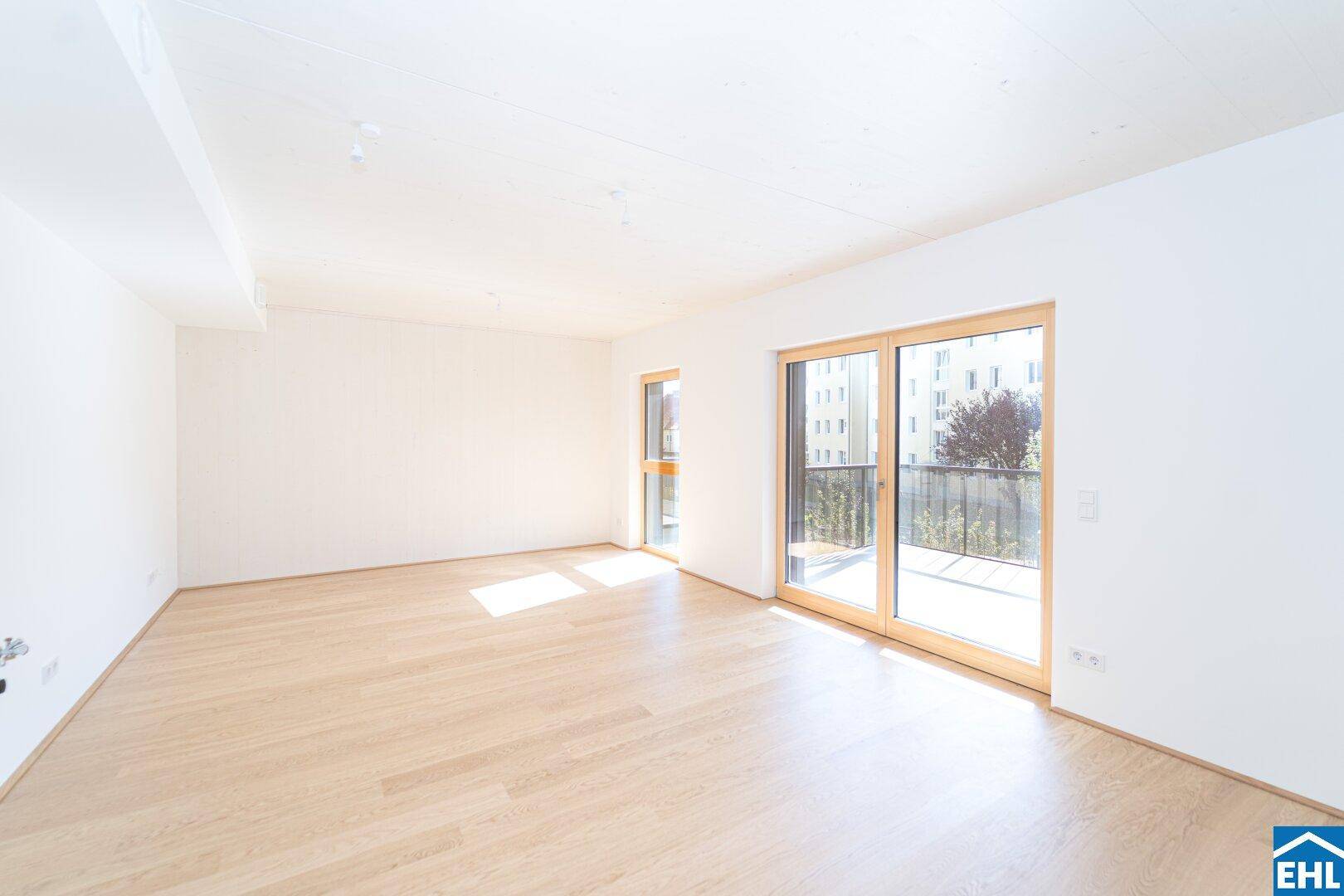 Helles, leeres Wohnzimmer mit hellem Holzfußboden und großzügigem Zugang zum Balkon.