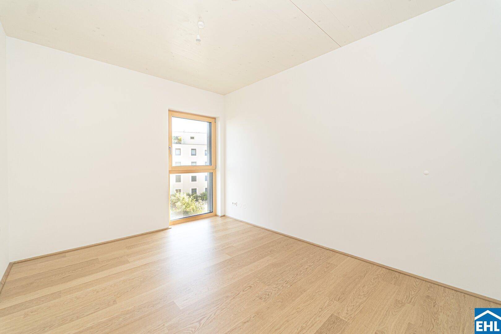 Ruhiges Schlafzimmer mit hellem Parkettboden und großem Fenster für viel Tageslicht.