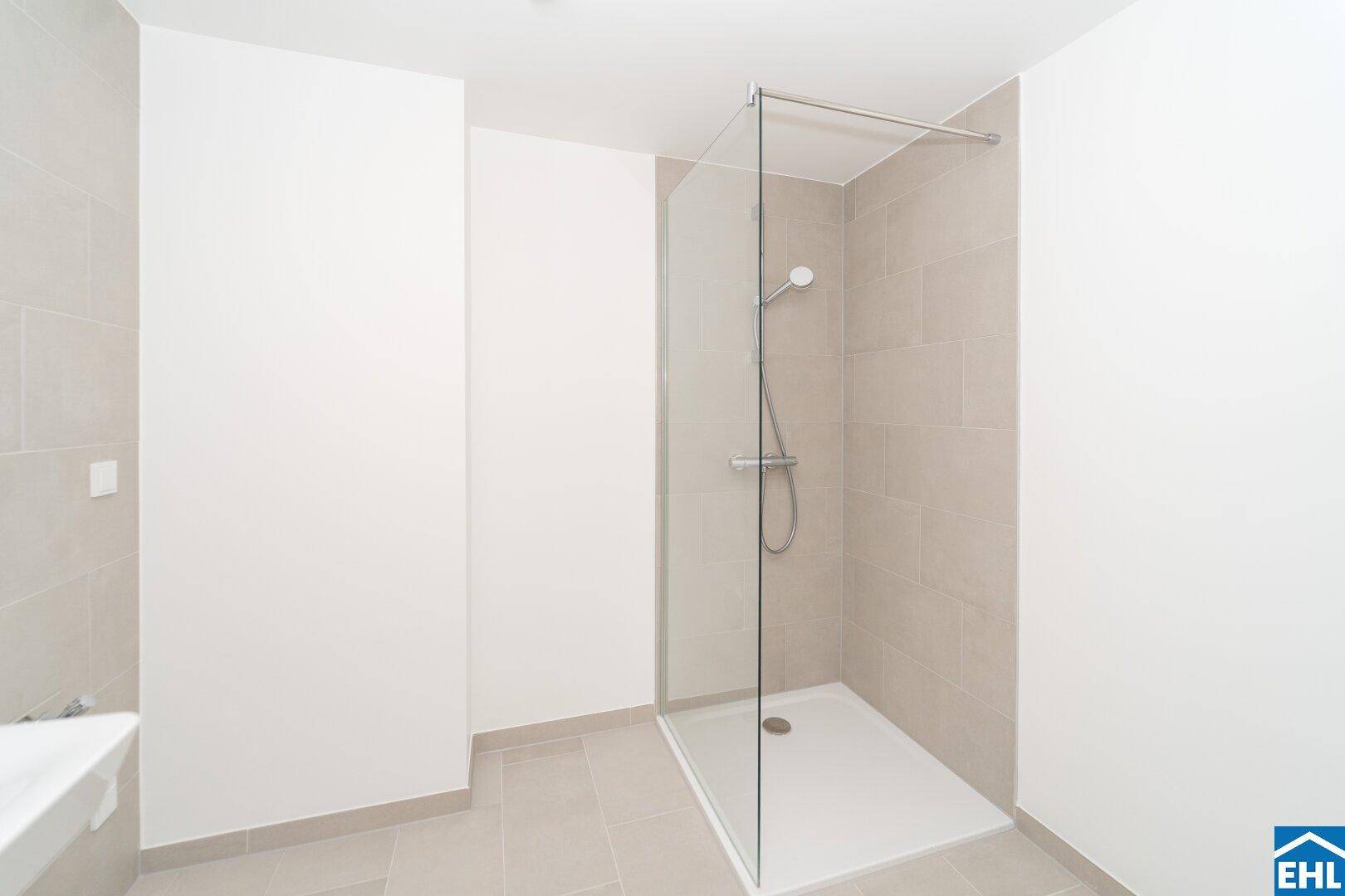 Modernes Badezimmer mit begehbarer Dusche und hellen Fliesen an Wänden und Boden.
