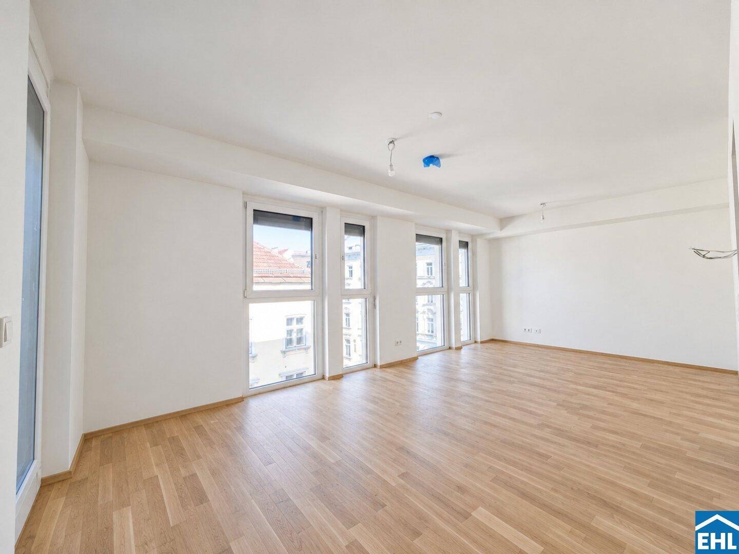 Heller, leerer Raum mit Laminatboden und großen Fenstern, die einen Blick auf die Umgebung bieten.