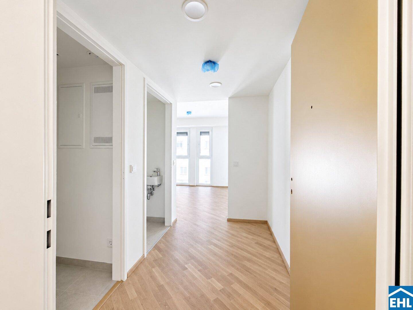 Heller Flur mit Laminatboden und Zugang zu verschiedenen Räumen, inklusive einem kleinen Waschbecken.