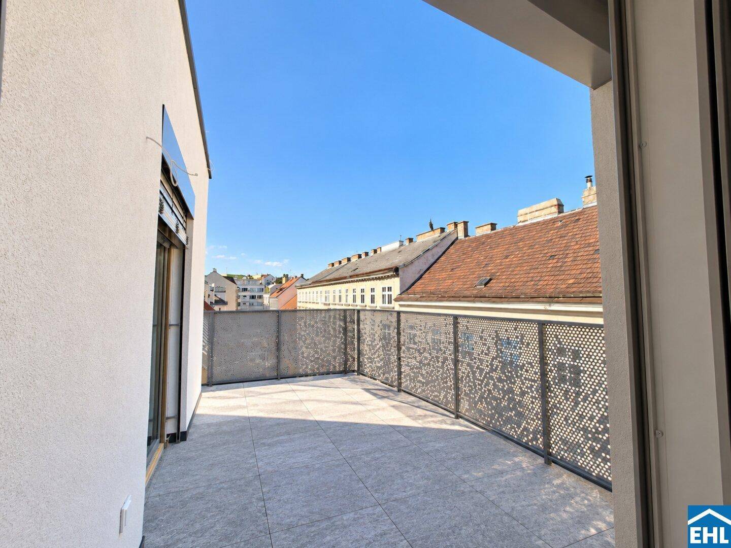 Große, geflieste Terrasse mit Metallgeländer und Blick auf die umliegenden Dächer der Stadt.