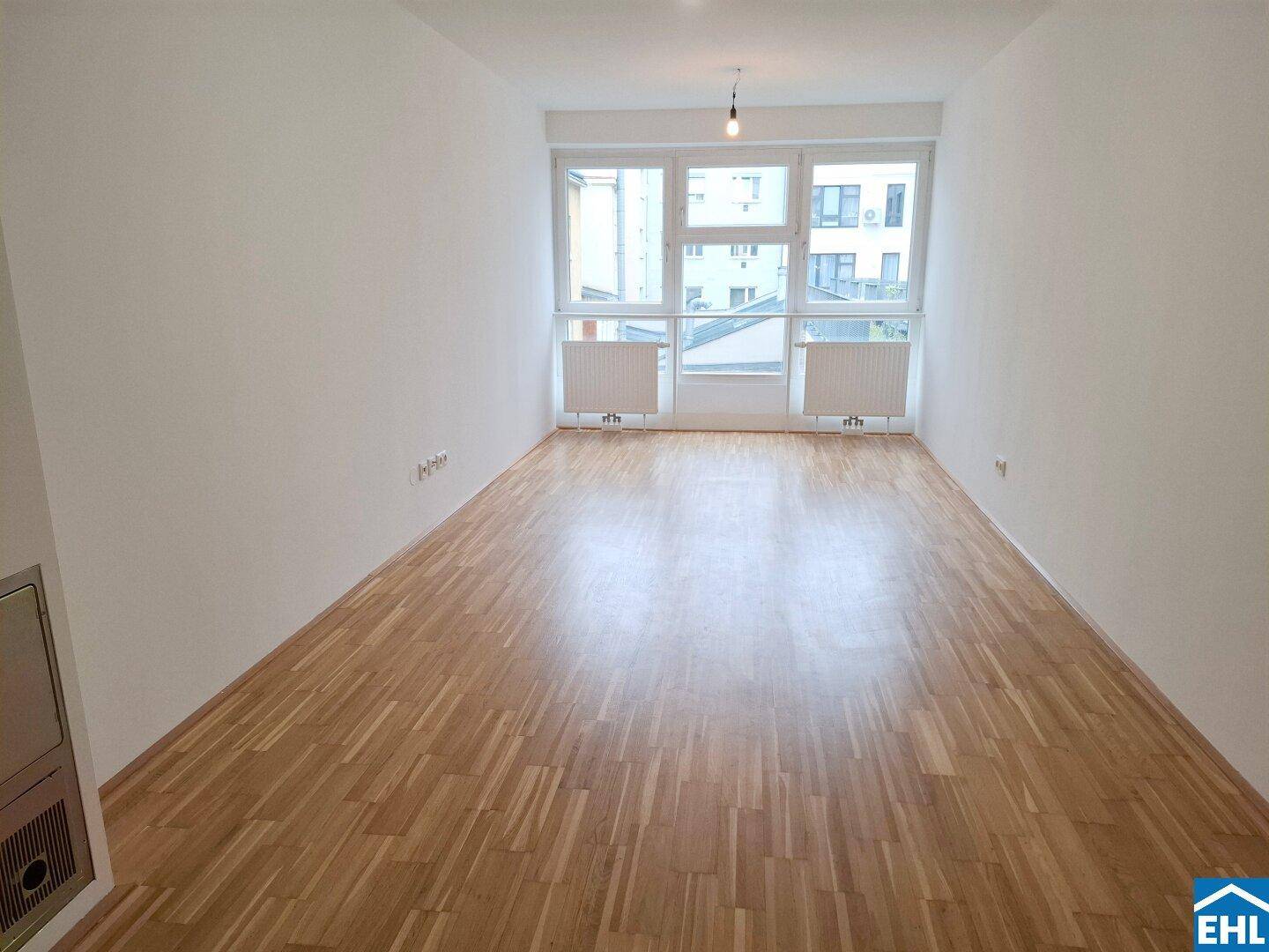 Helles Wohnzimmer mit Parkettboden und großen Fenstern, die viel Tageslicht hereinlassen.