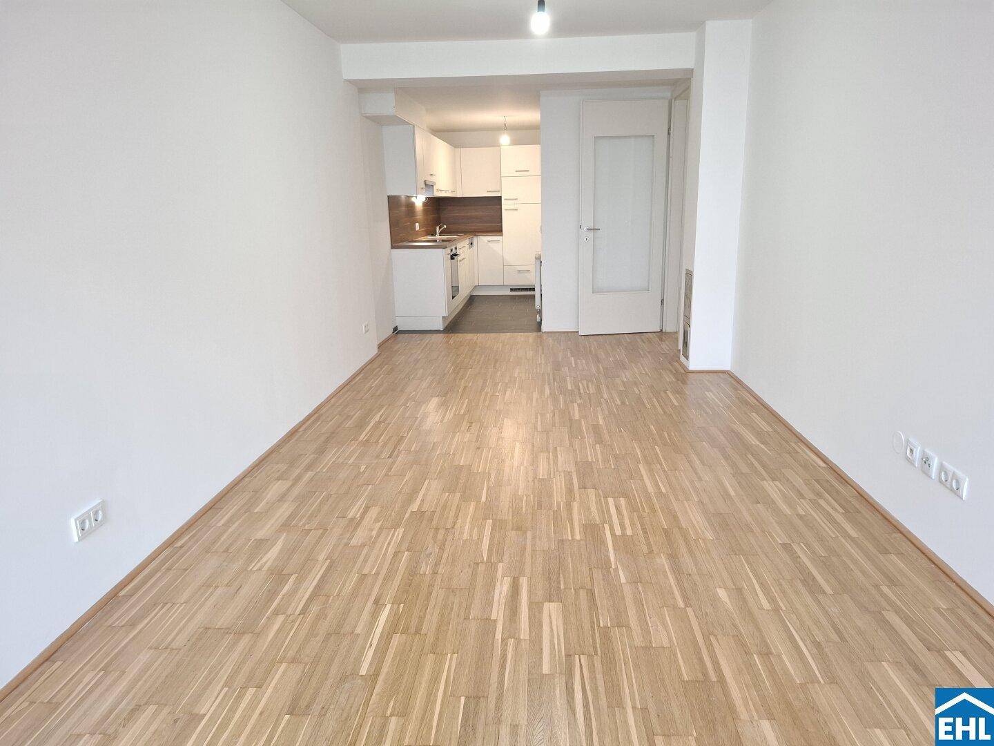 Geräumiges Wohnzimmer mit Parkettboden und offenem Zugang zur angrenzenden modernen Küche.