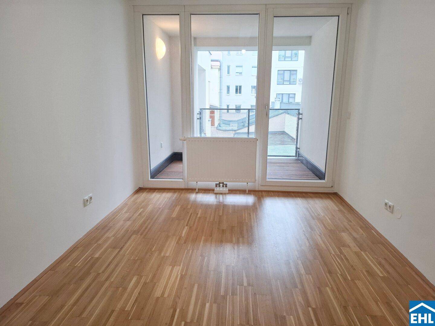 Heller Raum mit Parkettboden und Zugang zu einem französischen Balkon mit Gittergeländer.