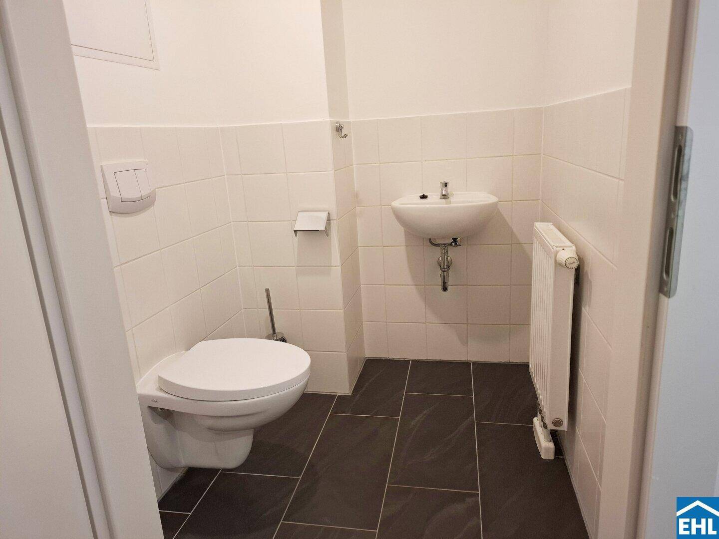 Kleines Gäste-WC mit Wand-WC, Waschbecken und dunklen Bodenfliesen in modernem Stil.