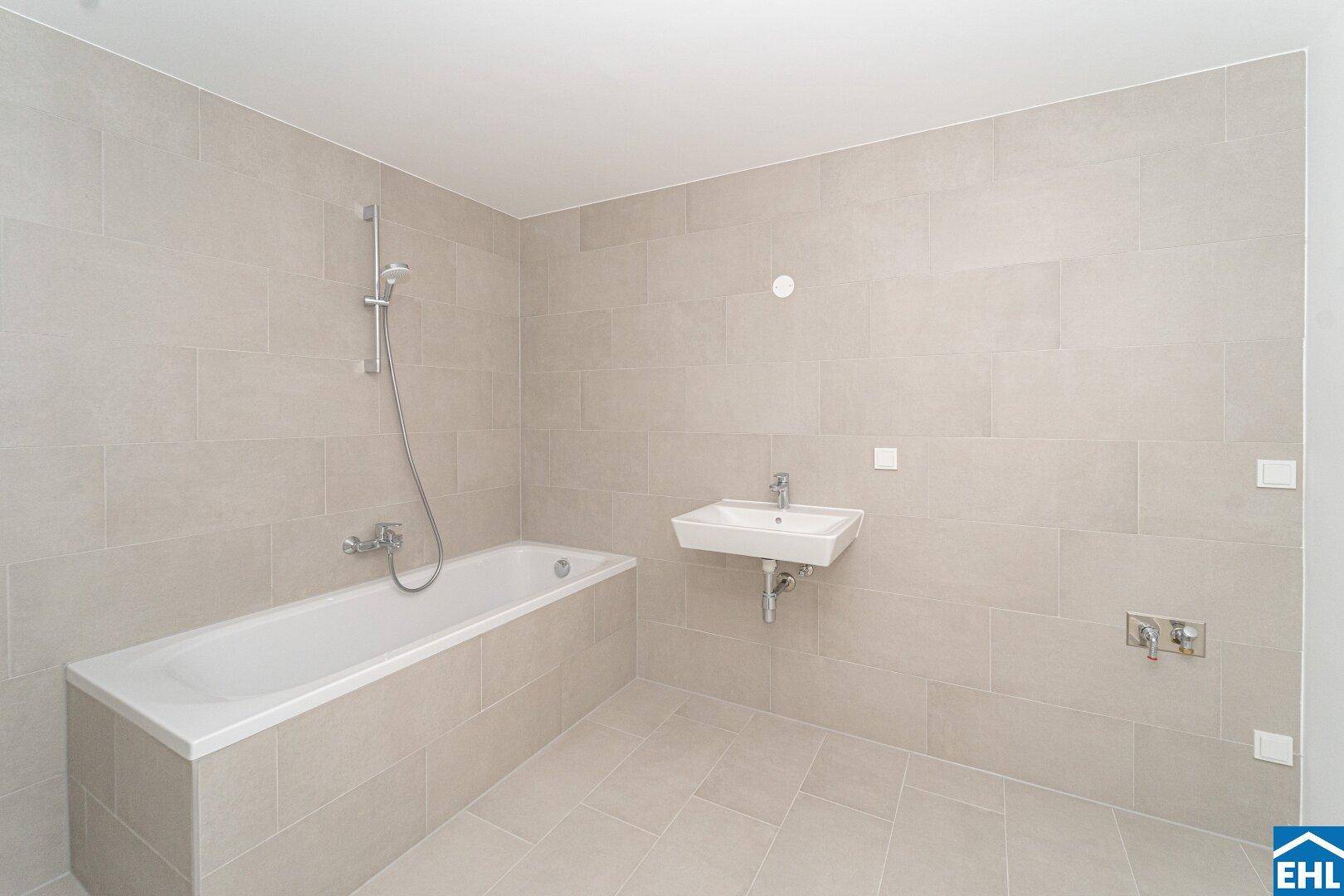 Helles Badezimmer mit Badewanne, Waschbecken und modernen, großformatigen Fliesen.