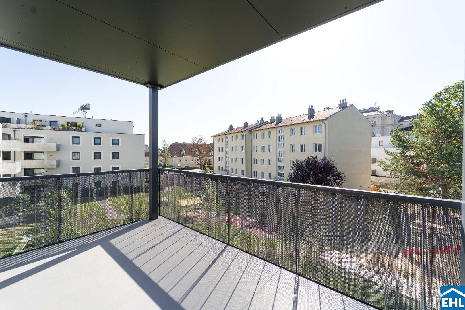 Heller Balkon mit Blick auf eine gepflegte Grünanlage und weitere Wohngebäude.