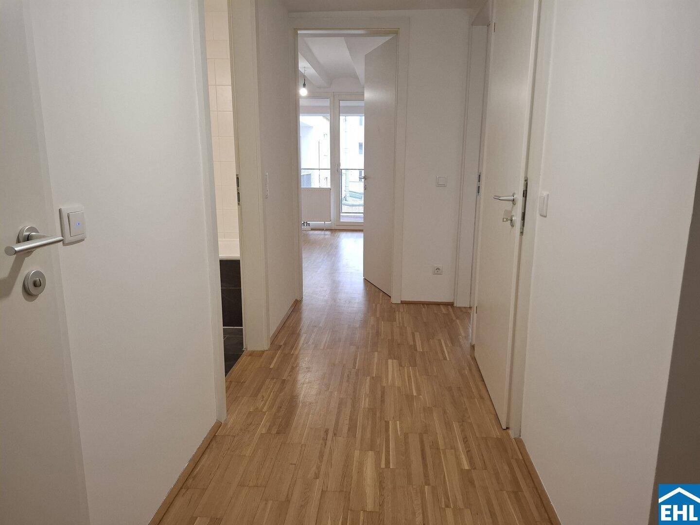 Heller Flur mit Parkettboden, der zu verschiedenen Wohnbereichen und einem Balkon führt.