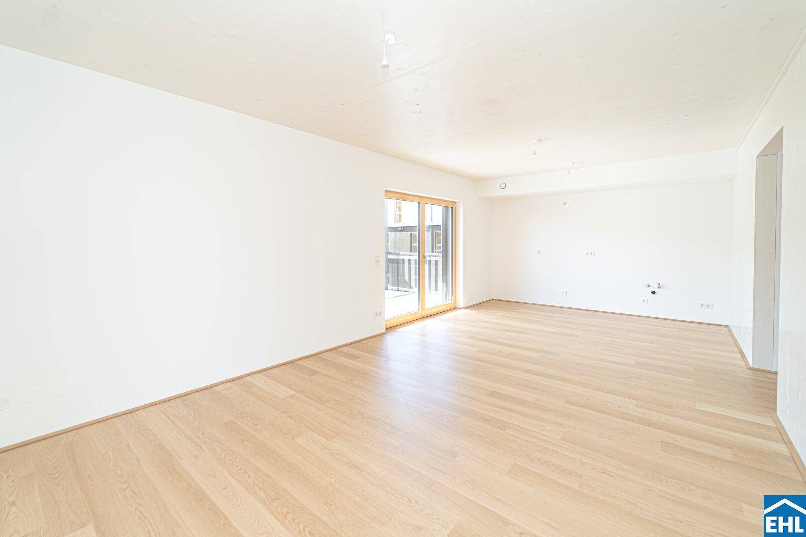 Geräumiges, leeres Wohnzimmer mit hellem Parkettboden und Zugang zu einem Balkon.