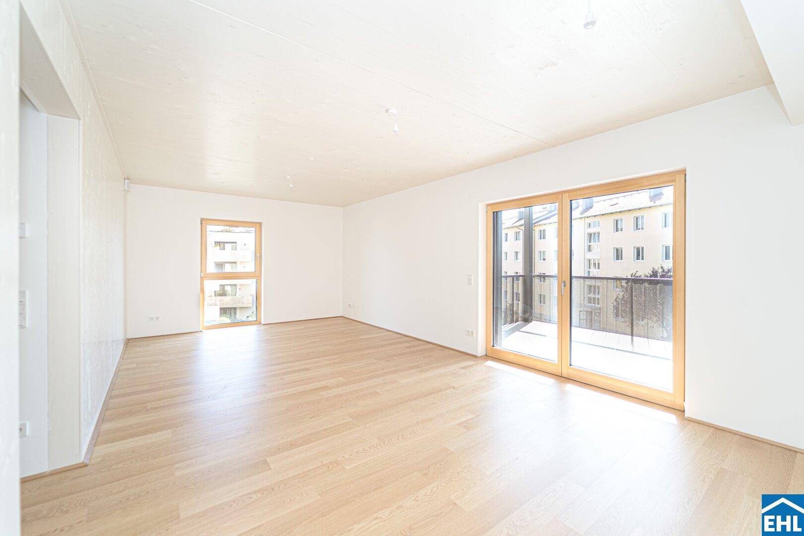 Lichtdurchflutetes Wohnzimmer mit Holzboden und großen Fenstern, die viel Tageslicht hereinlassen.